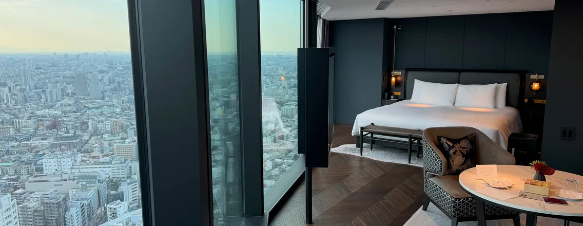 Hotelkamer met kingsize bed en een raamwand die uitkijkt over de daken van Tokyo