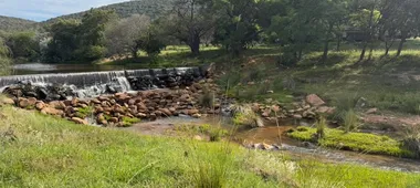 Een riviertje met een lage stuw in het bosveld van de Waterberg, met heuvels op de achtergrond