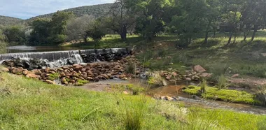 Een riviertje met een lage stuw in het bosveld van de Waterberg, met heuvels op de achtergrond