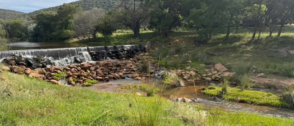 Een riviertje met een lage stuw in het bosveld van de Waterberg, met heuvels op de achtergrond