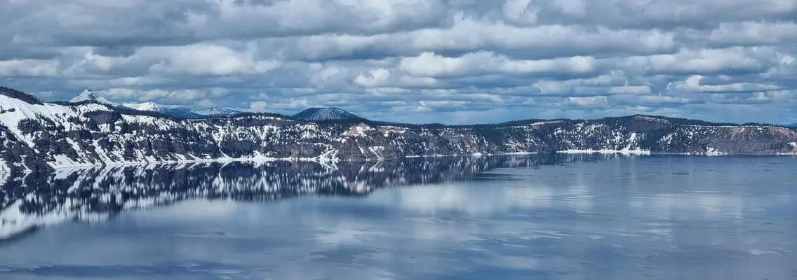 Crater Lake in Oregon met sneeuw op de kraterwand en wolken weerspiegeld in het water