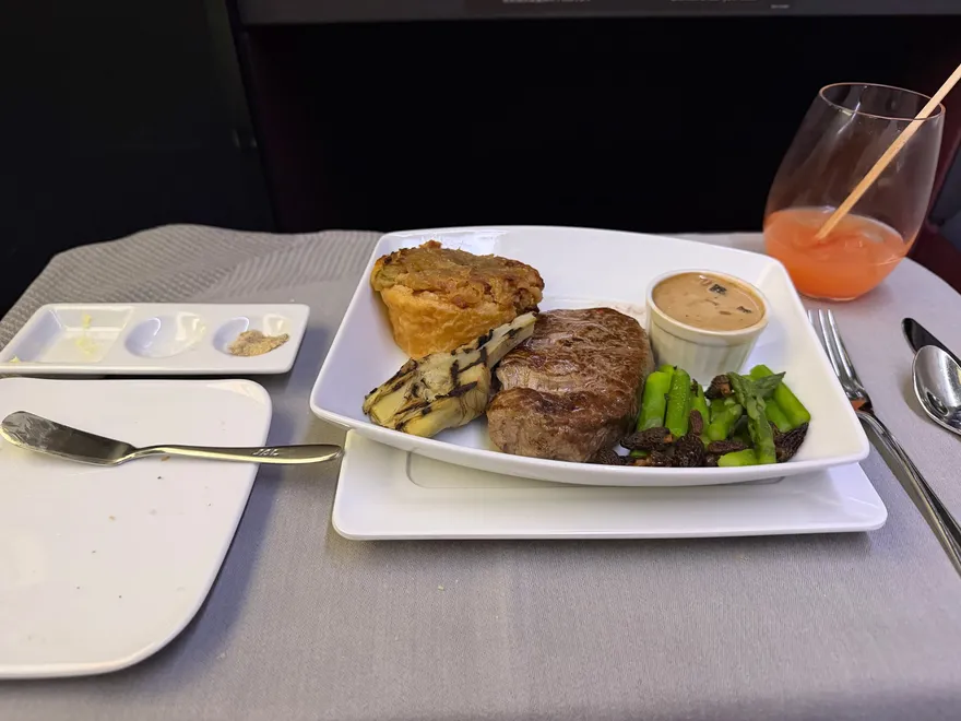 Hoofdgerecht met vlees, asperges en saus op een gedekt tafeltje in businessclass