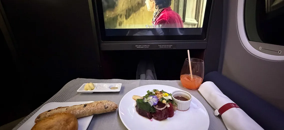 Tafeltje in businessclass met voorgerecht, stokbrood en een scherm, onderweg naar Tokyo