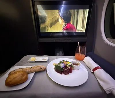 Tafeltje in businessclass met voorgerecht, stokbrood en een scherm, onderweg naar Tokyo
