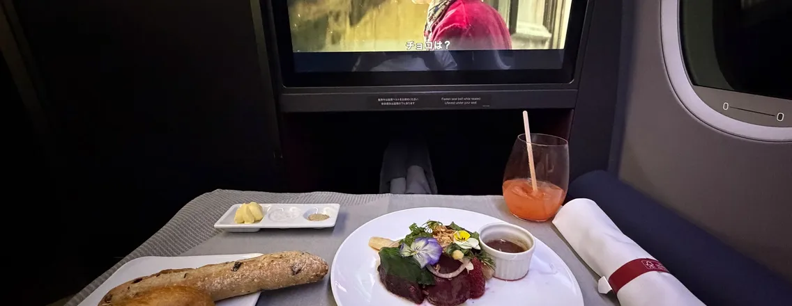 Tafeltje in businessclass met voorgerecht, stokbrood en een scherm, onderweg naar Tokyo
