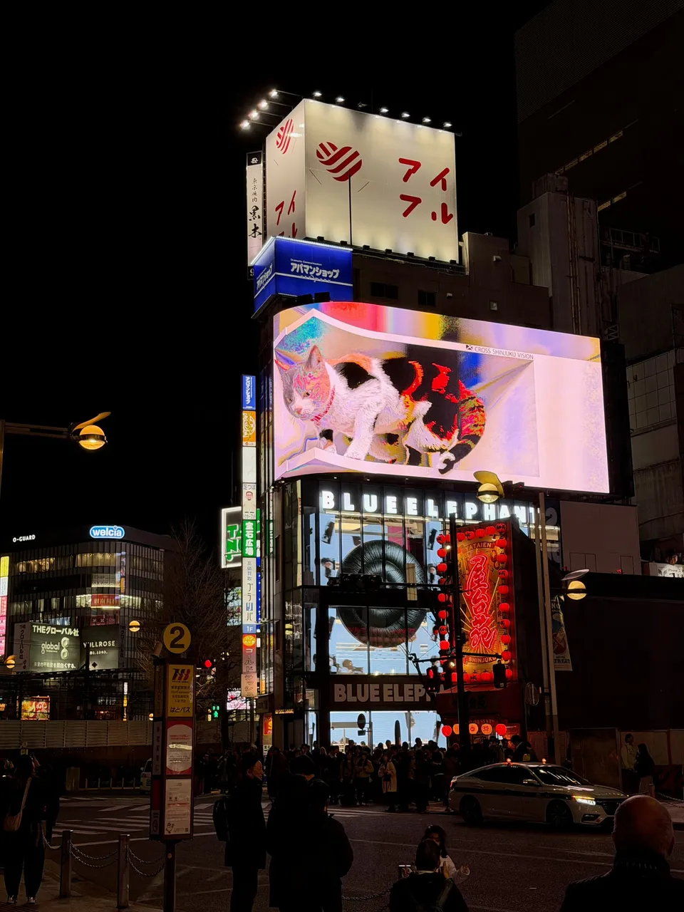 Het gebogen scherm met de driedimensionale kat boven een kruising in Shinjuku bij avond