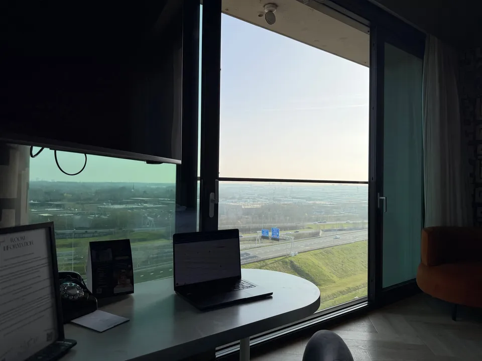 Laptop op een ronde tafel voor het hoge raam van de hotelkamer in Best