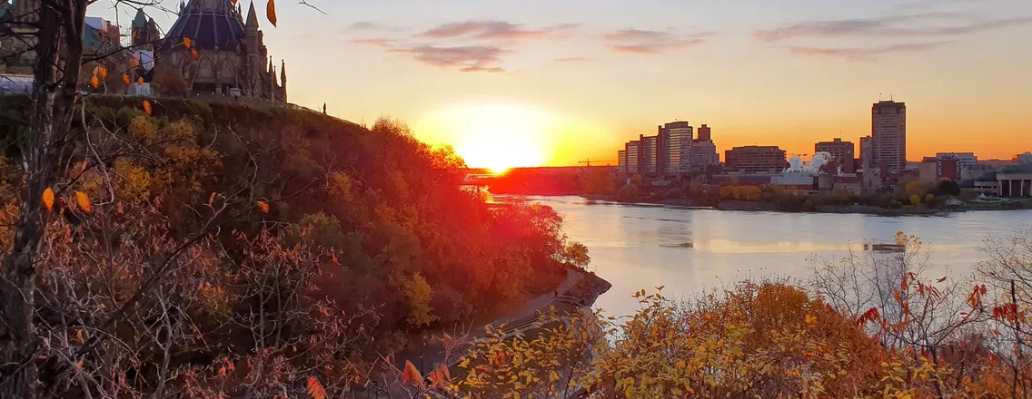 De parlementsgebouwen van Ottawa bij zonsondergang boven de rivier