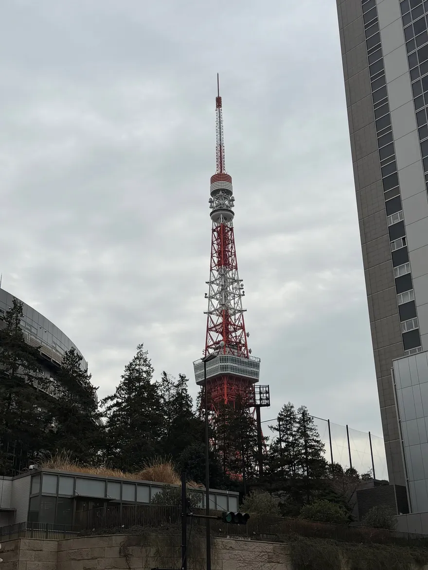 Tokyo Tower in rood en wit gezien vanaf straatniveau tussen de bomen door