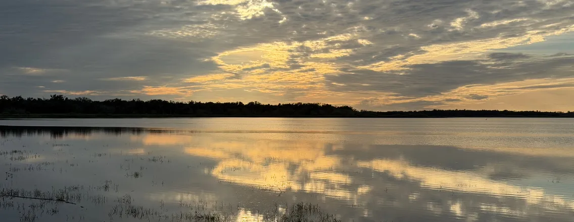 Zonlicht door wolken boven stil water bij Myakka in december
